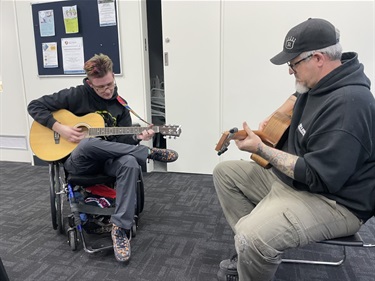 Two SIAG members playing guitar together, sharing a musical moment.