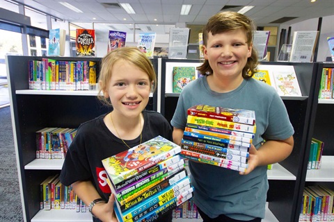 Two children posing for a photo holding books in a library