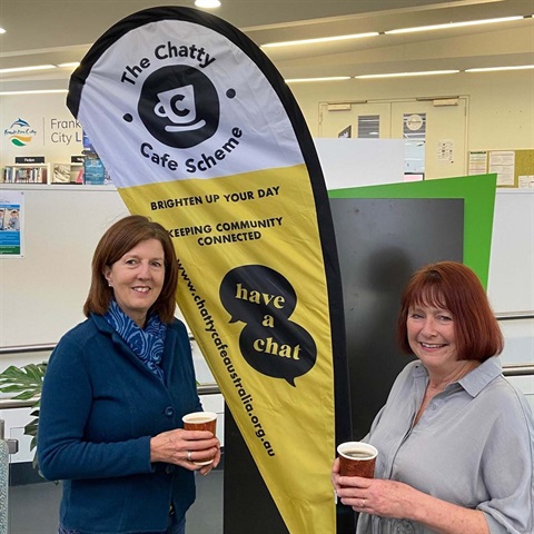 Two people drinking coffee in front of chatty cafe sign